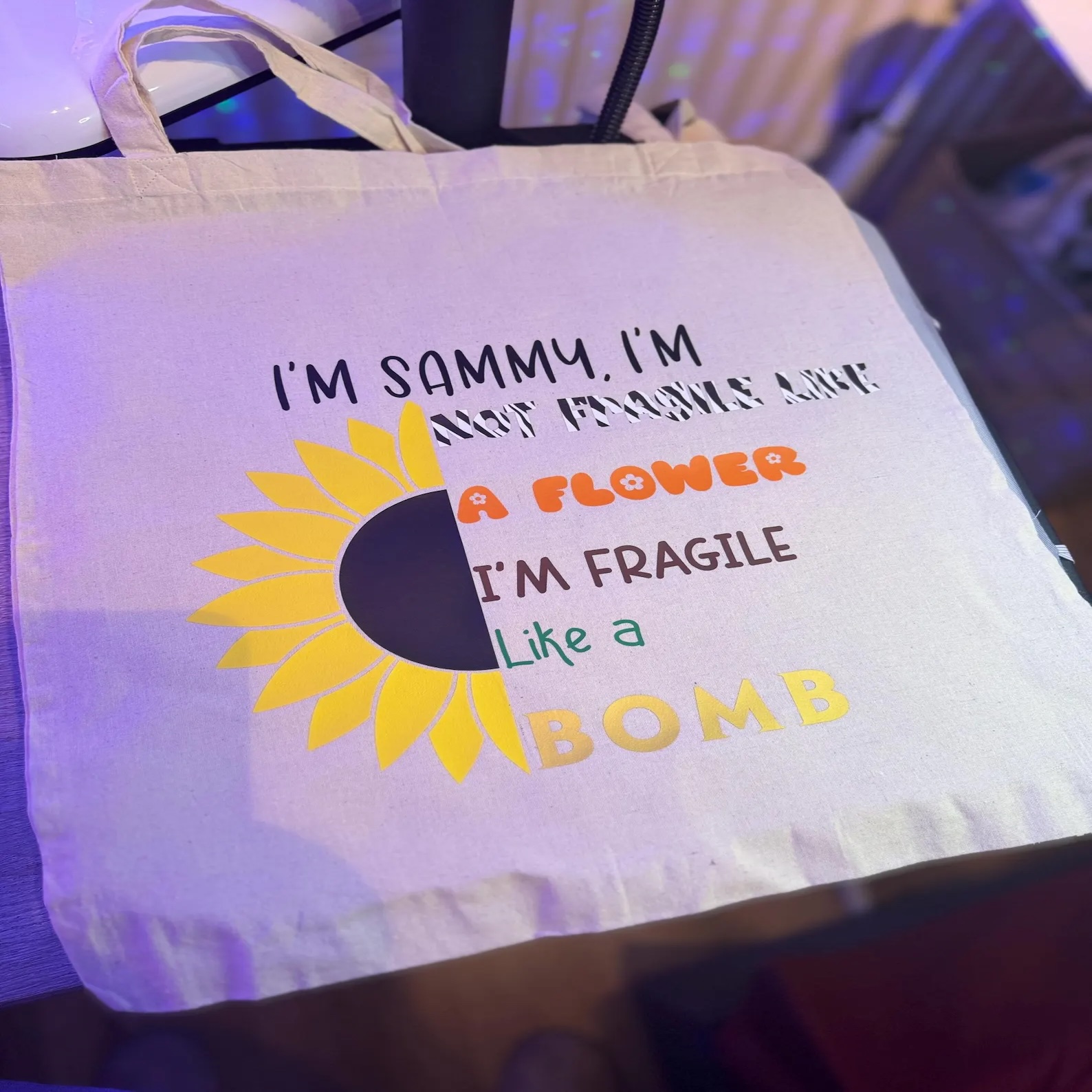 Tote bag with sunflower graphic with printed text 'I'm Sammy, I'm not fragile like a flower, I'm fragile like a bomb.'