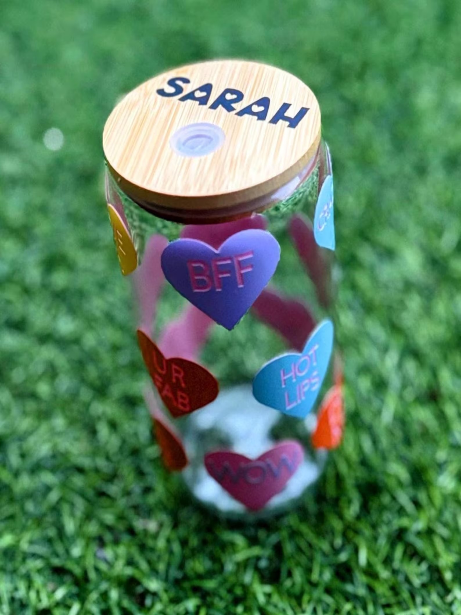 Handmade glass tumbler with multicoloured hearts and text inside such as 'BFF', 'WOW' and more with personalised name on top of the wooden lid.