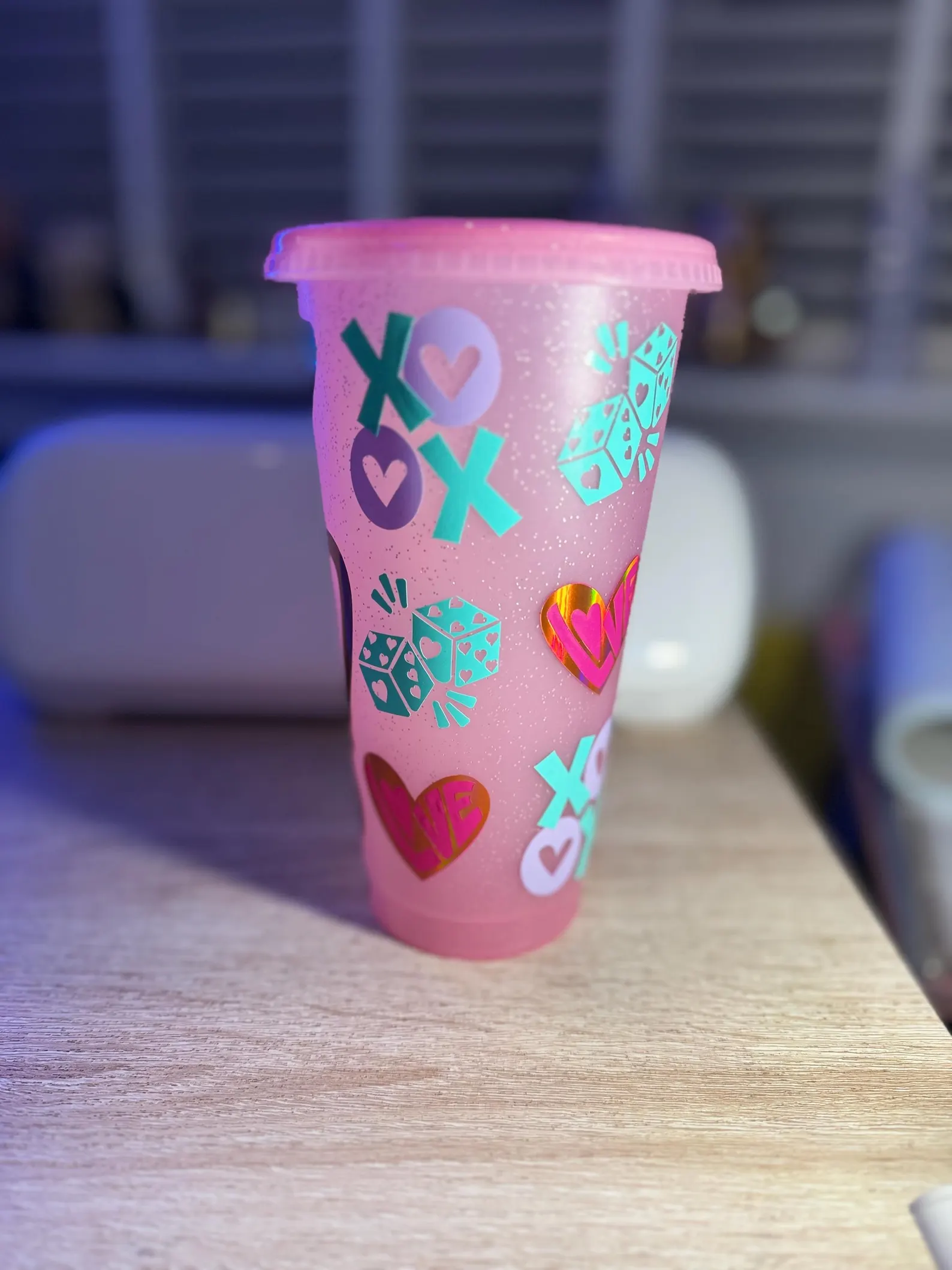Pink glitter cup with pink, blue and purple sticker graphics of hearts, crosses and die.